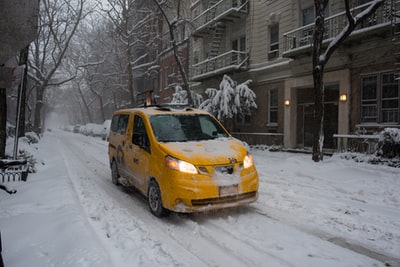 During the day, the yellow car in the snow covered roads
